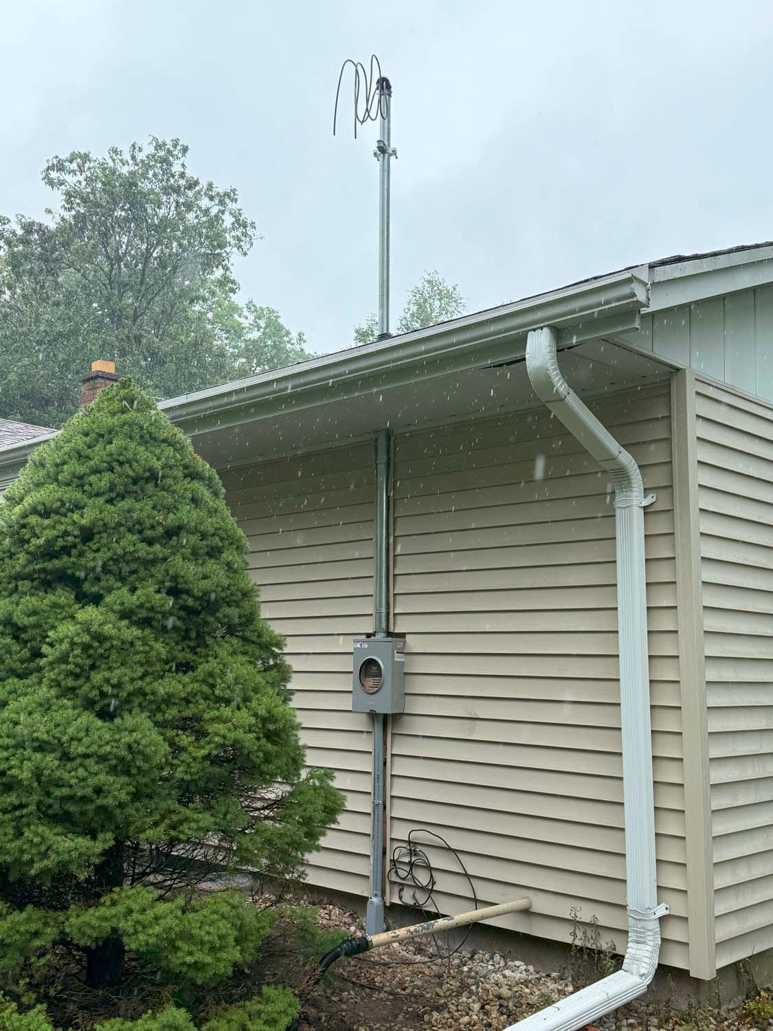 Exterior electrical meter box on a light-colored house with a metal conduit running up the side.