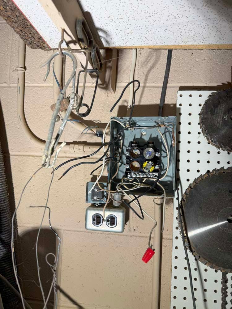 Exposed electrical wiring and box with a double outlet, mounted on a brick wall in a workshop.