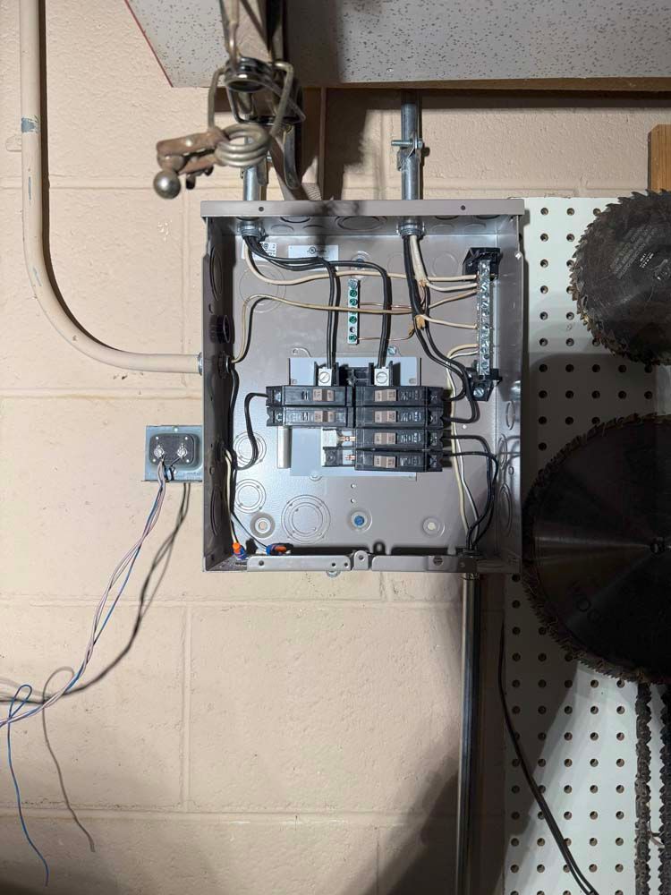 Electrical panel mounted on a light beige wall with exposed wires and conduits, next to saw blades.