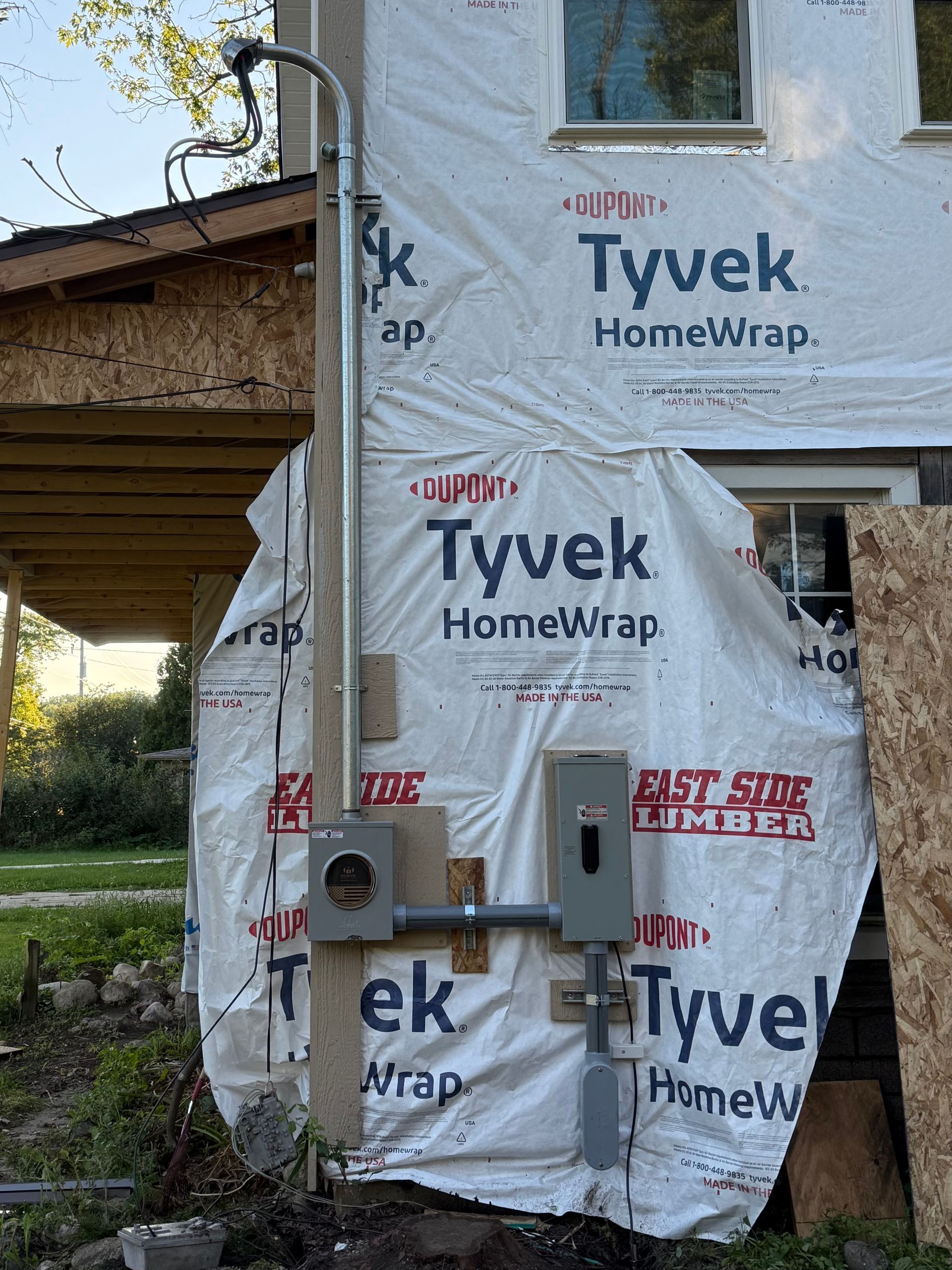 Electrical panel and conduit mounted on a building with Tyvek wrap; gray and white.