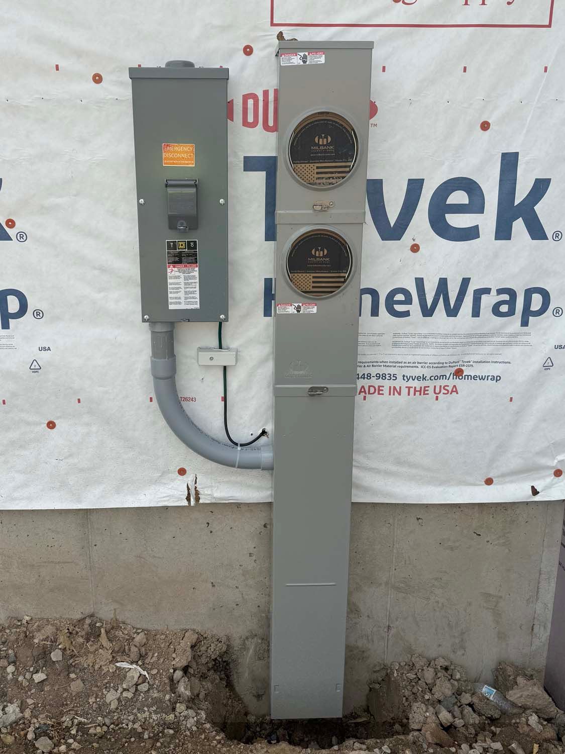 Gray electrical panel and meter base mounted on a building's exterior.