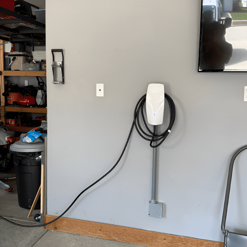 Electric vehicle charger mounted on a gray garage wall with a coiled cable.