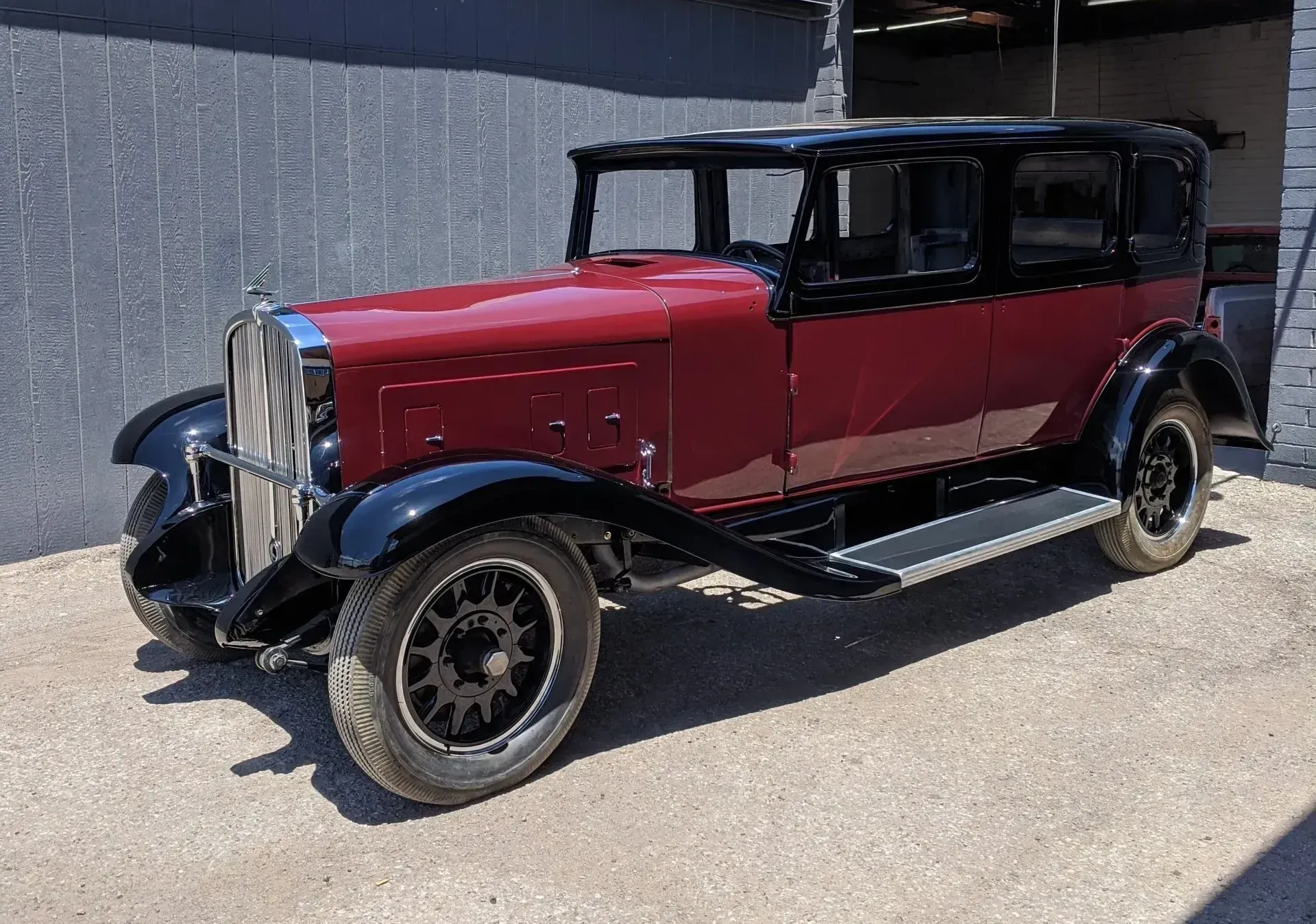 An old red car is parked in front of a building.