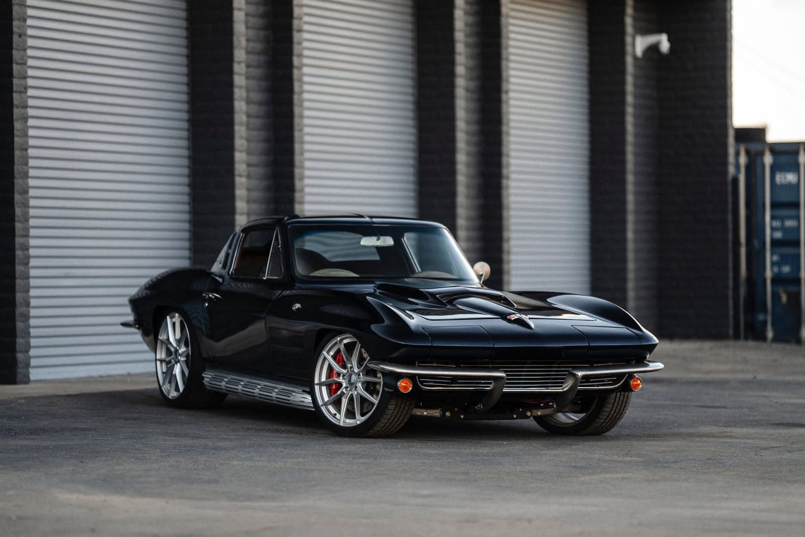 A black corvette is parked in front of a garage door.