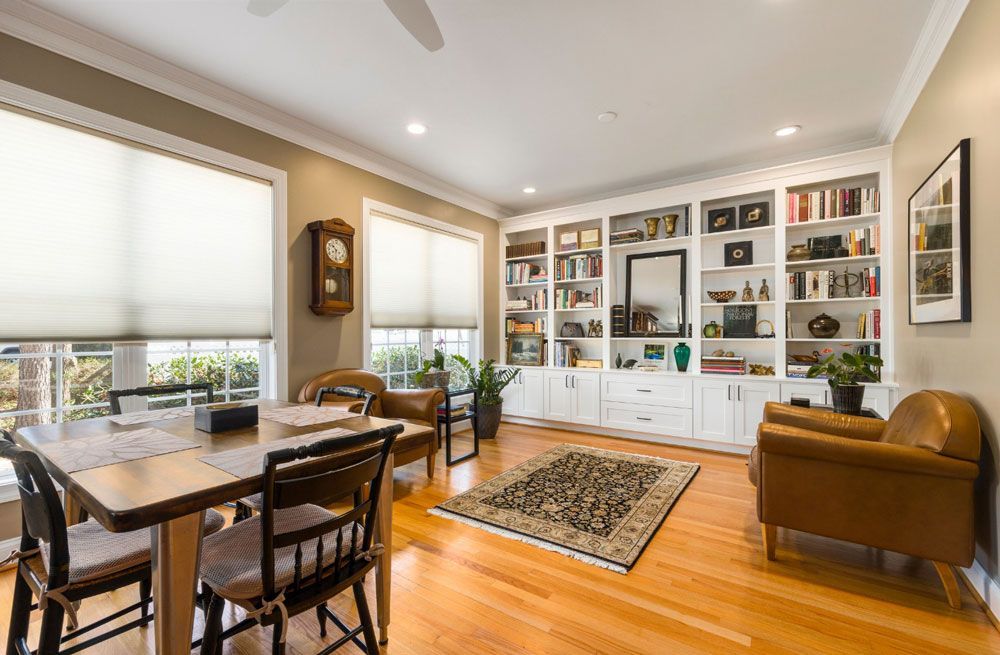 A living room with hardwood floors , a dining table , chairs , bookshelves and a clock.