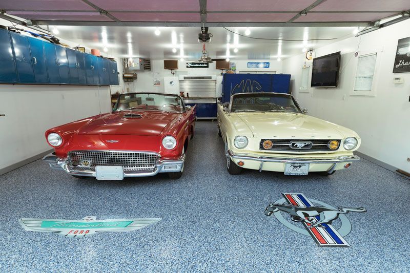 Two cars are parked in a garage with a mustang logo on the floor.