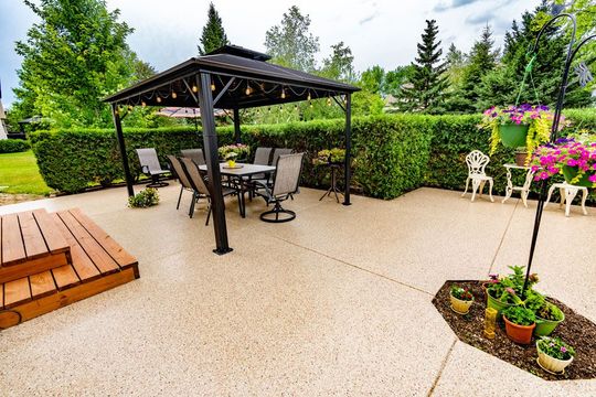 Patio with a gazebo, table, and chairs on a coated concrete surface.