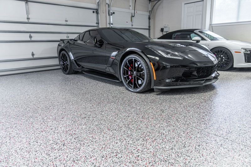 A black corvette is parked in a garage next to a white sports car.