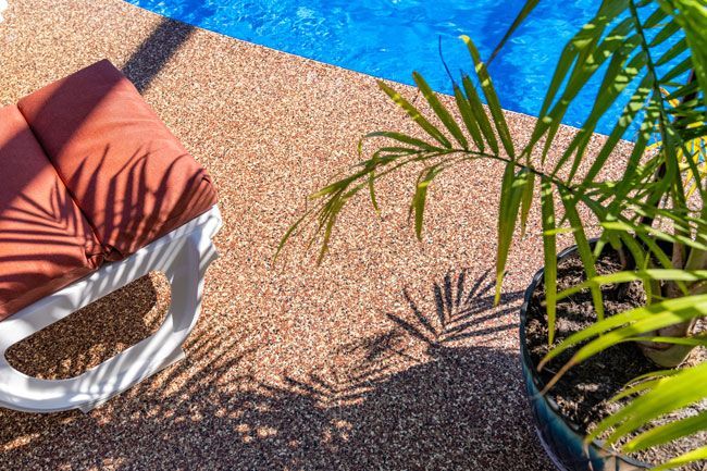 A chair is sitting next to a potted plant next to a swimming pool.