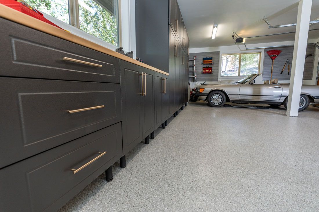 A car is parked in a garage with a lot of cabinets and drawers.