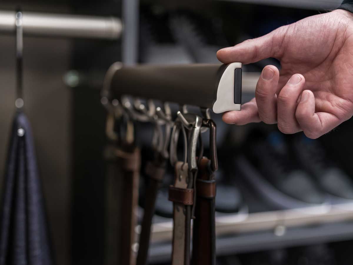 A bunch of belts are hanging on hooks in a closet