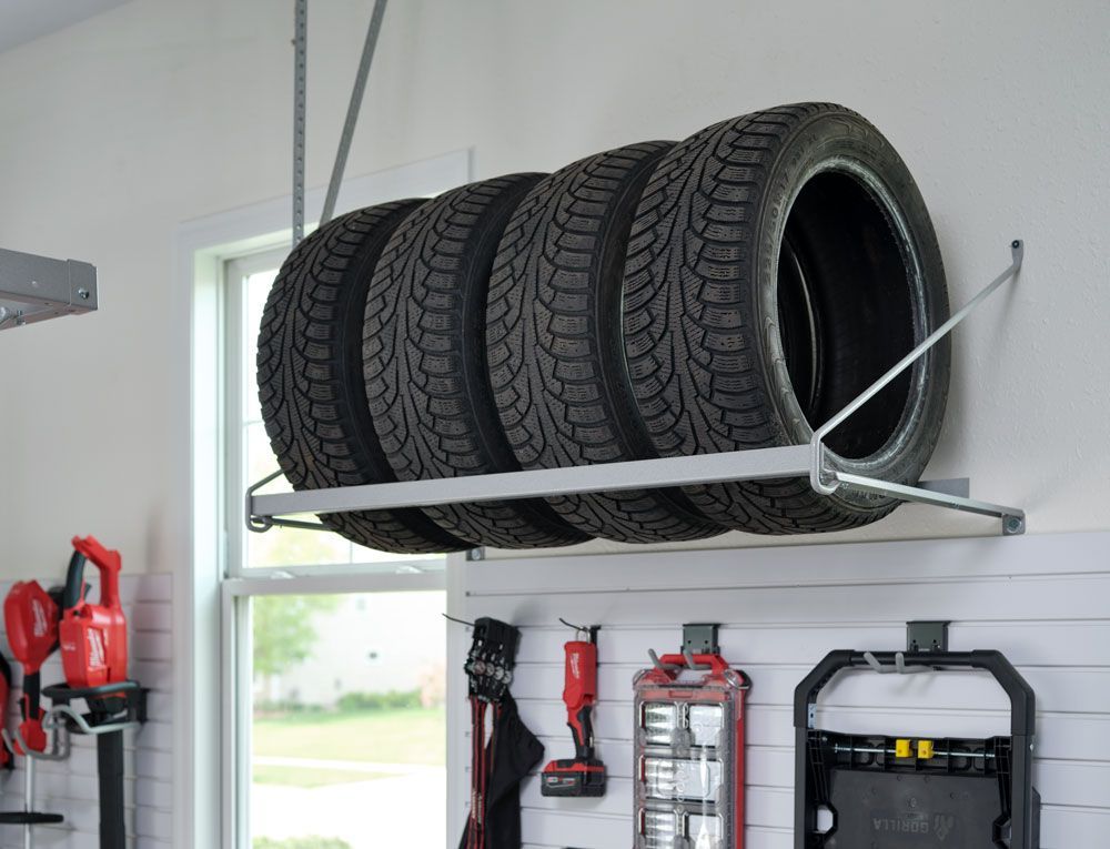 Four tires are stacked on top of each other on a rack in a garage.