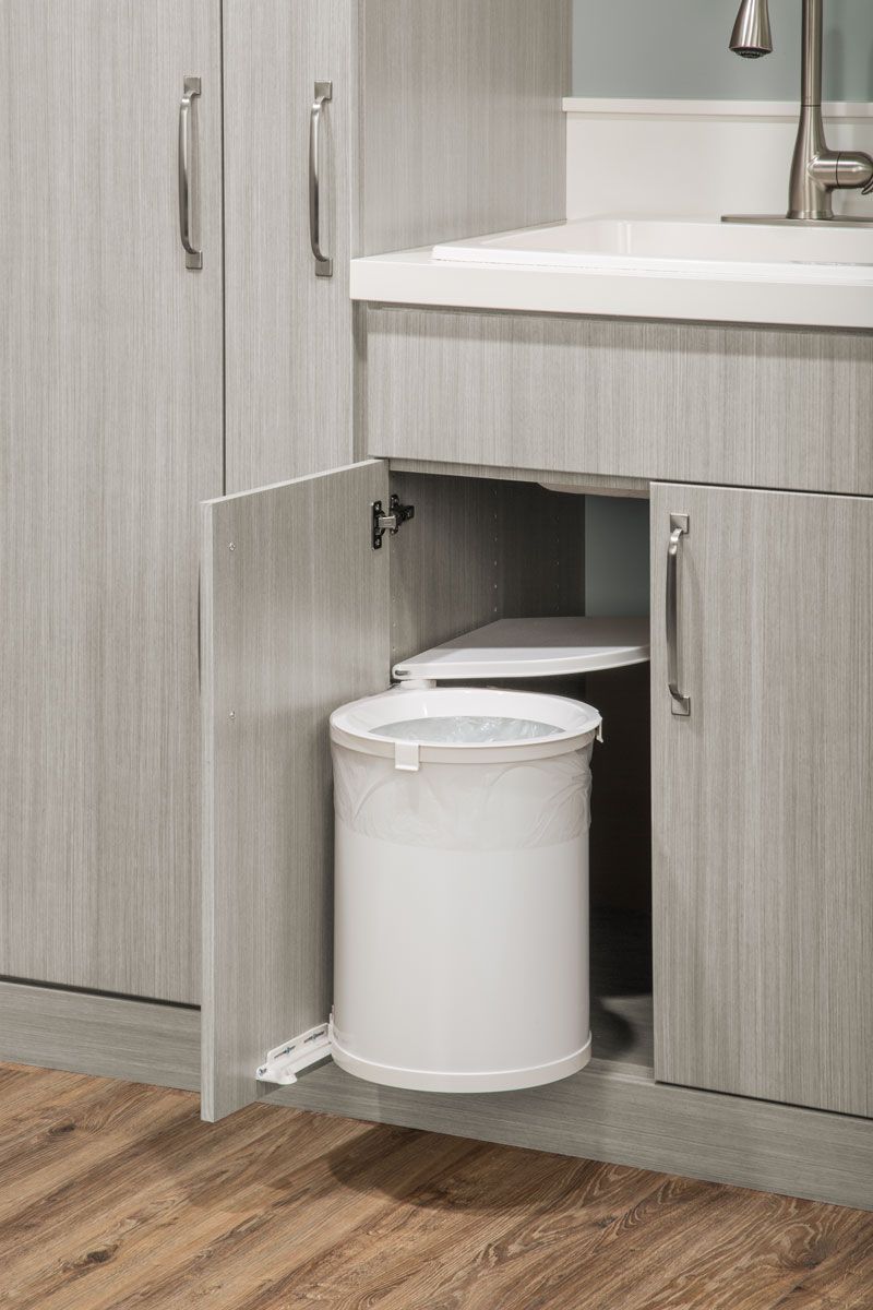 A white trash can is sitting under a sink in a laundry room.