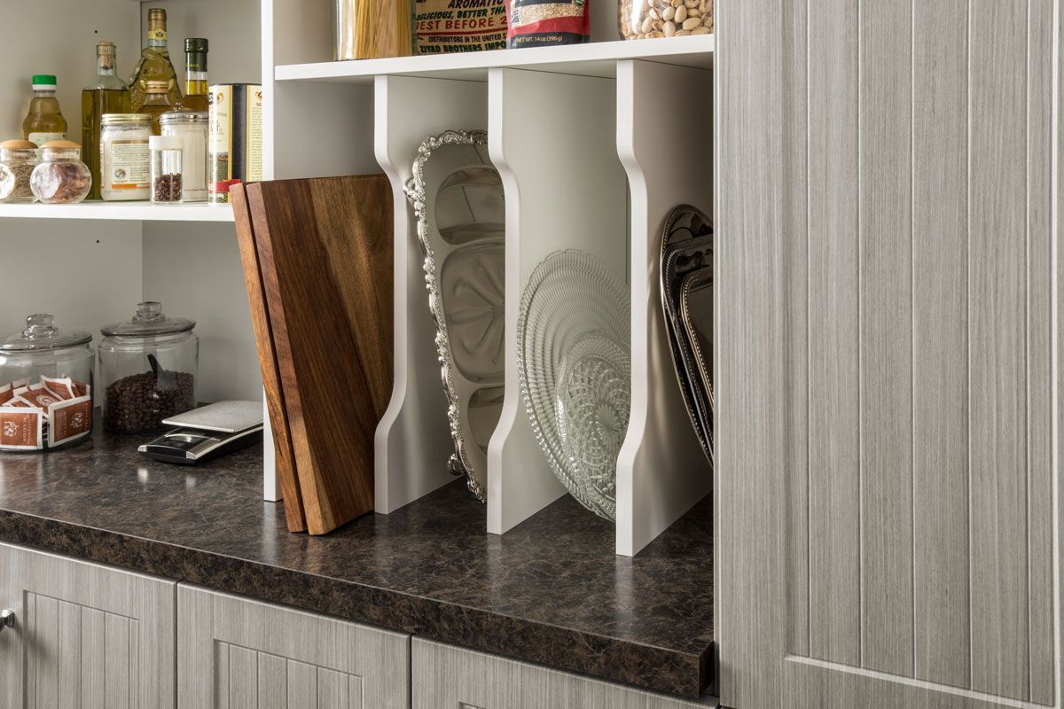 A kitchen pantry with a cutting board , plates , bowls and bottles on the shelves.