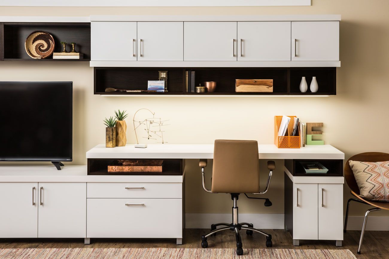 A home office with a desk , chair , television and cabinets.