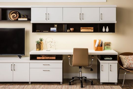 A home office with a desk , chair , television and cabinets.