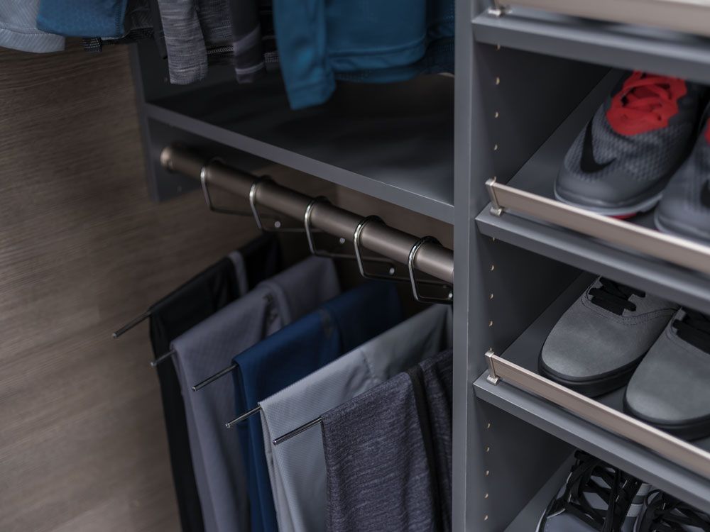 A closet with pants hanging on a rack and shoes on shelves.
