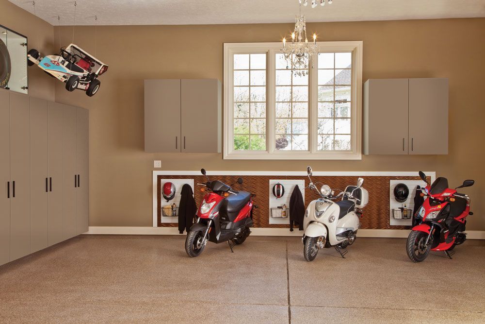 Three scooters are parked in a garage next to a window.