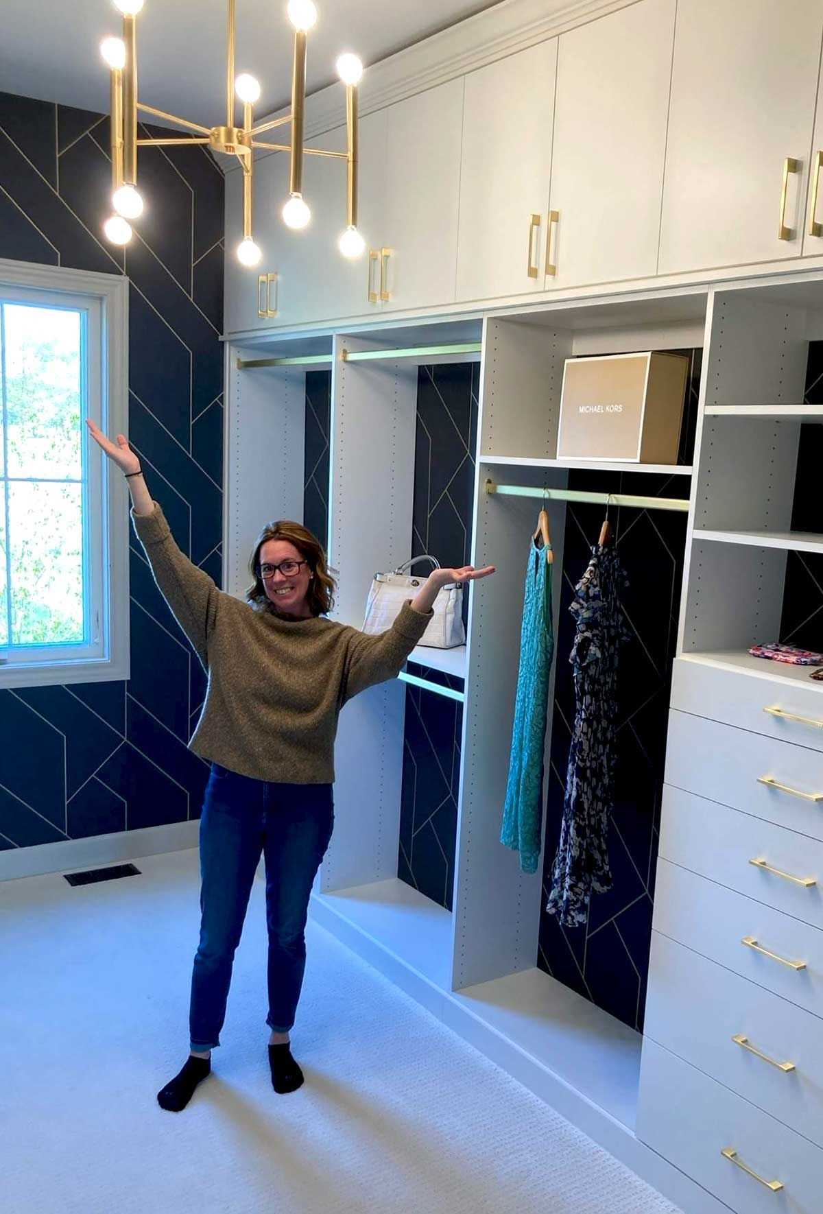 A persons is standing in a walk in closet with her arms outstretched.