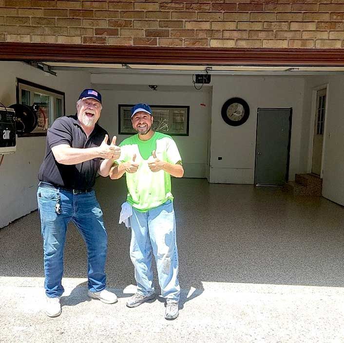 Two people are standing in a garage giving thumbs up.
