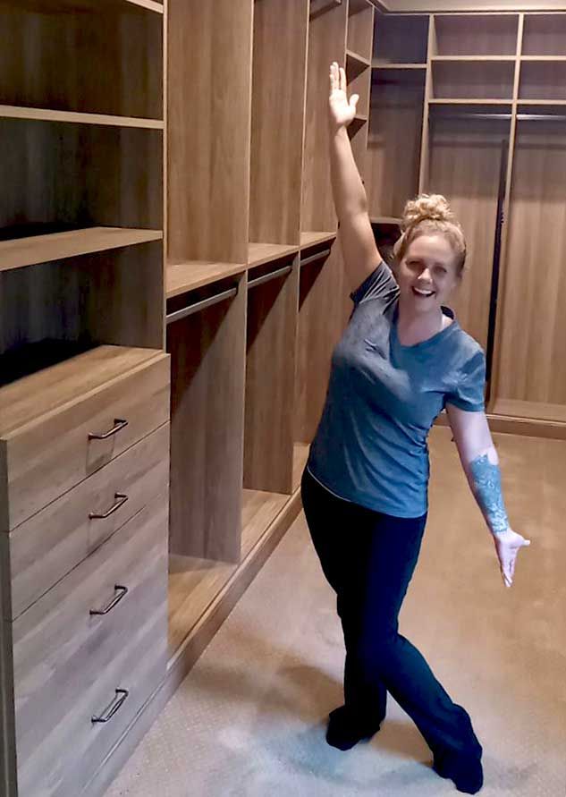 A person is standing in a walk in closet with her arms in the air.