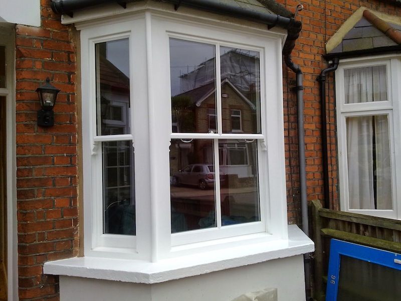 A white bay window is on the side of a brick building.