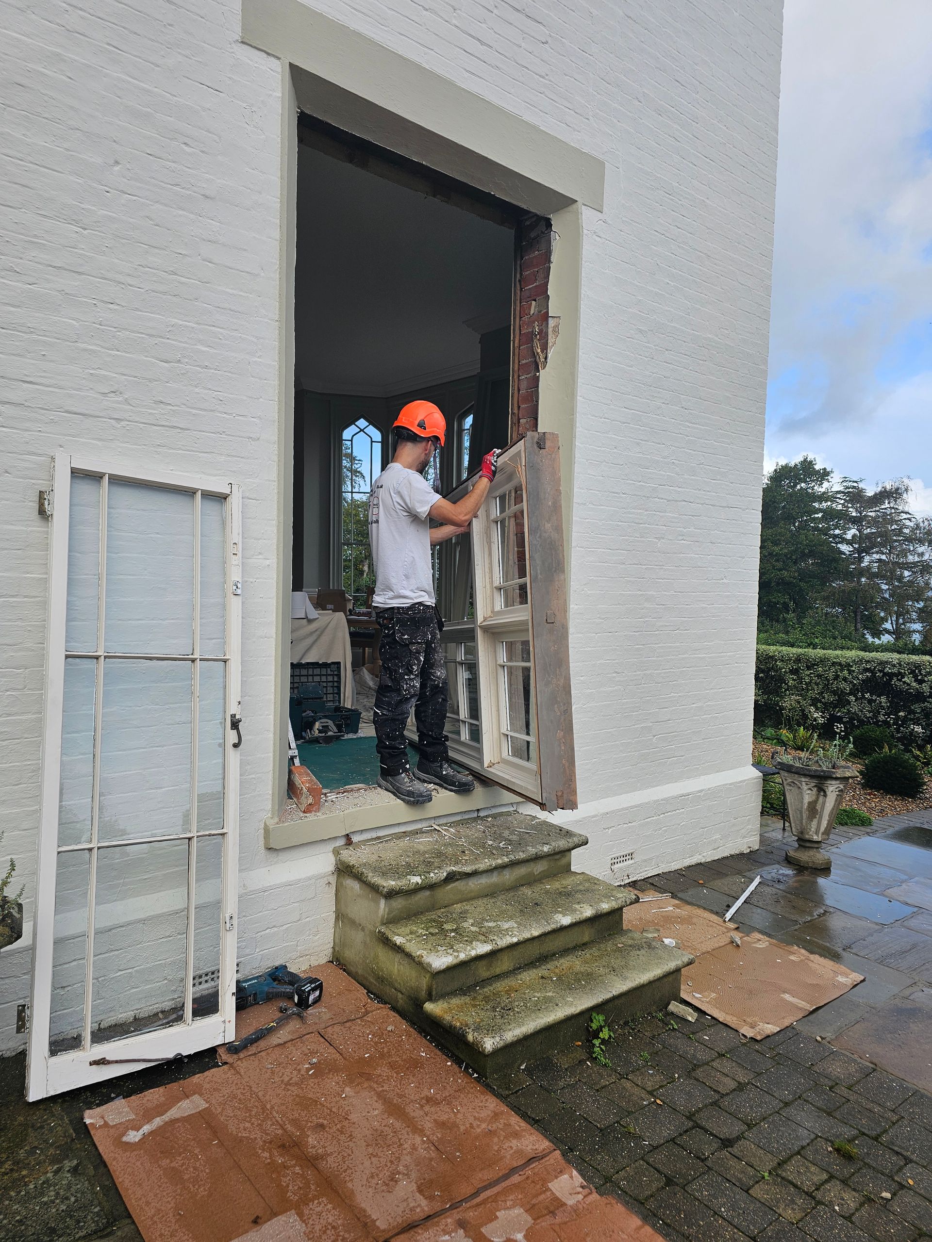 A man wearing a hard hat is standing in front of a white building.