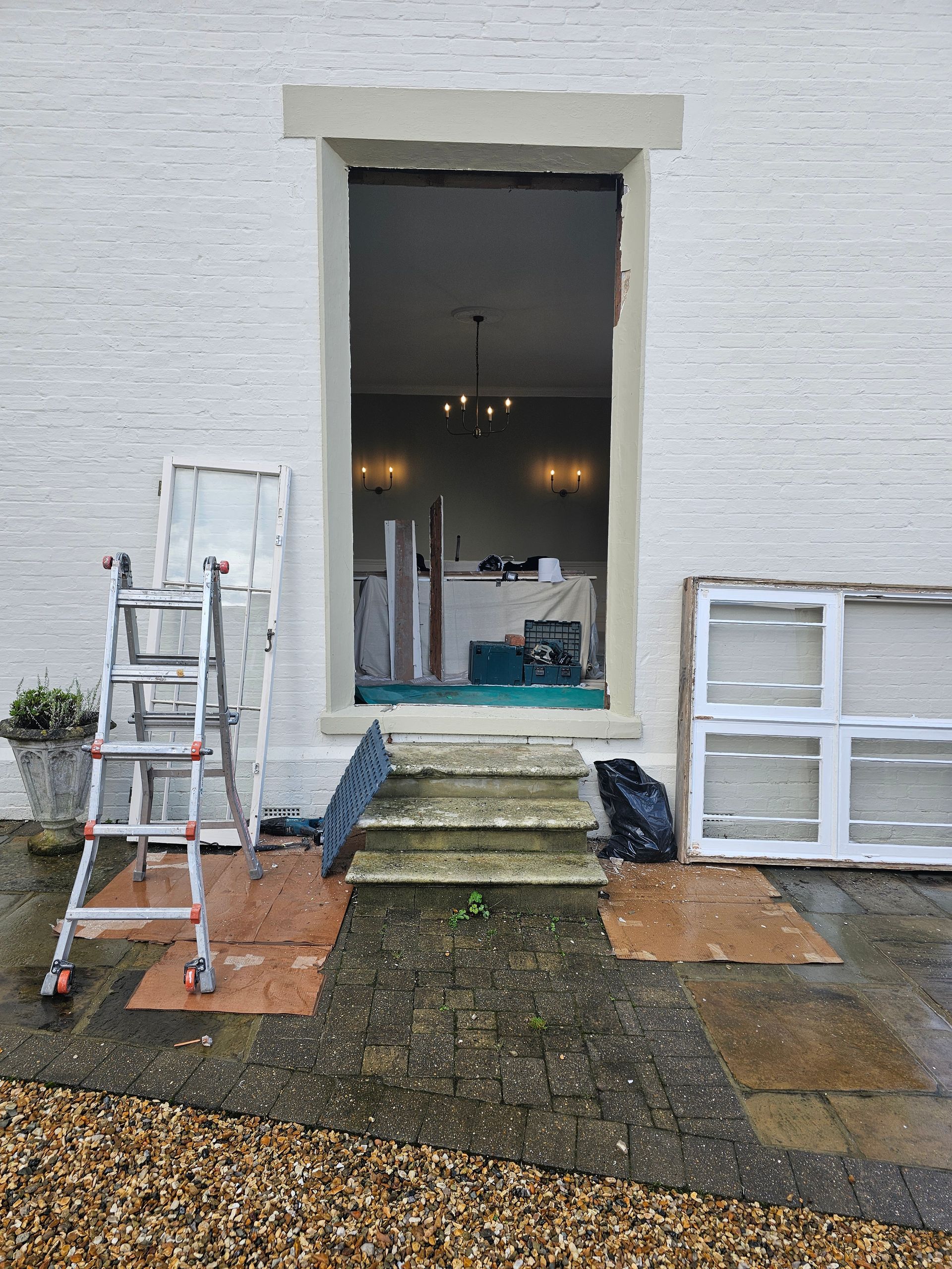 A ladder is sitting on the sidewalk in front of a white brick building.