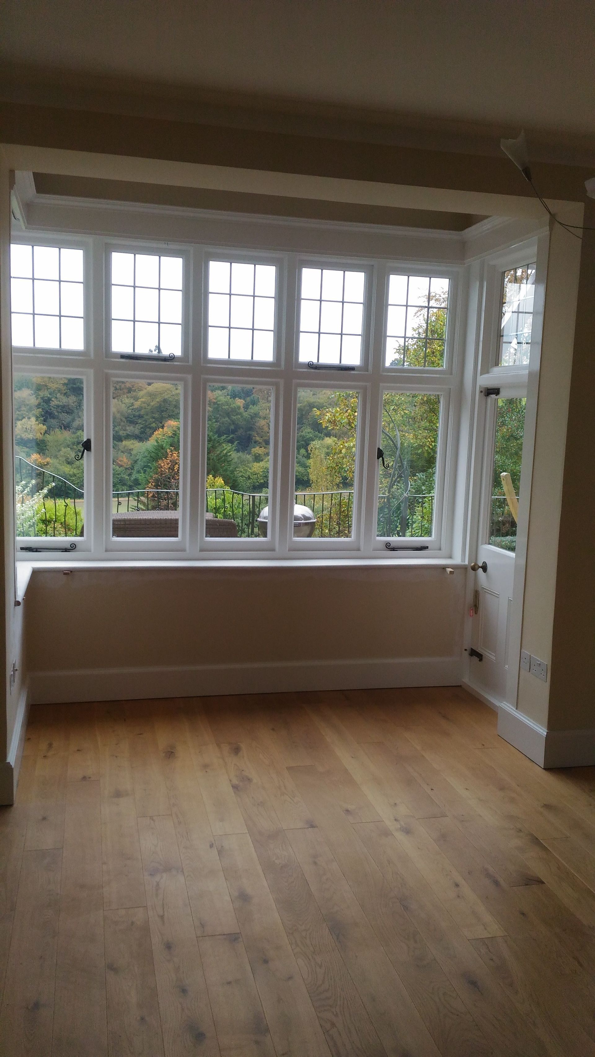 An empty room with a large window and hardwood floors.