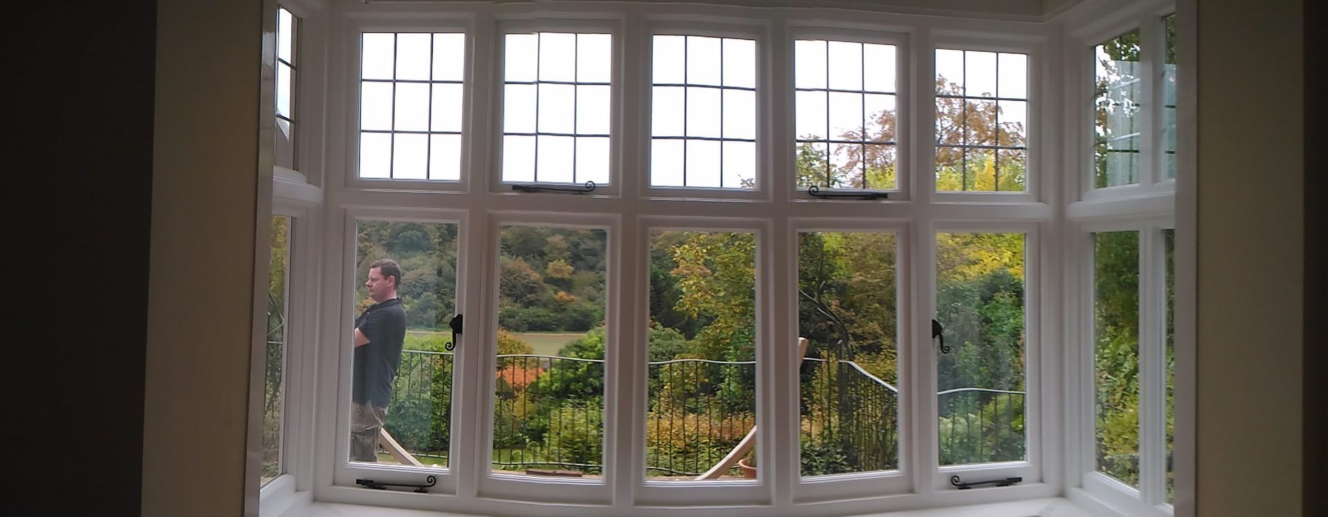 A man is standing in front of a large window looking out.