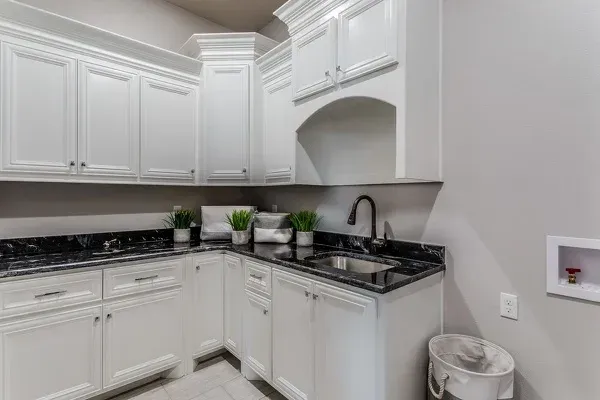 A laundry room with white cabinets , black counter tops , and a sink.