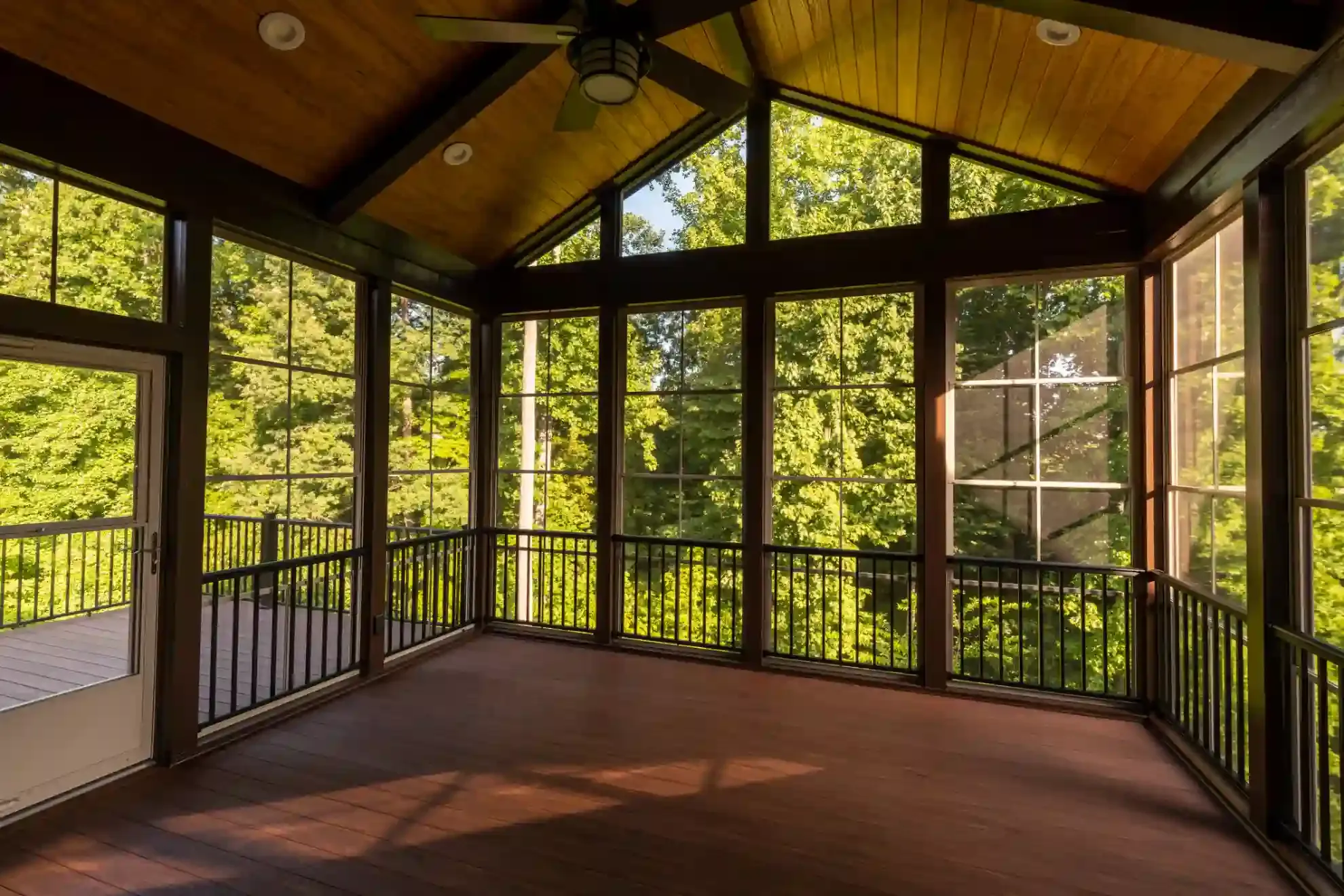 A screened in porch with a lot of windows and a ceiling fan.
