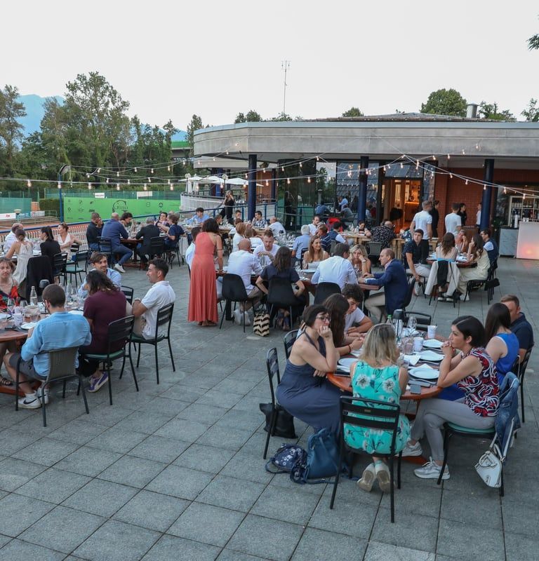 Ritrovo serale all'aperto con persone sedute ai tavoli, che socializzano e mangiano in un patio.