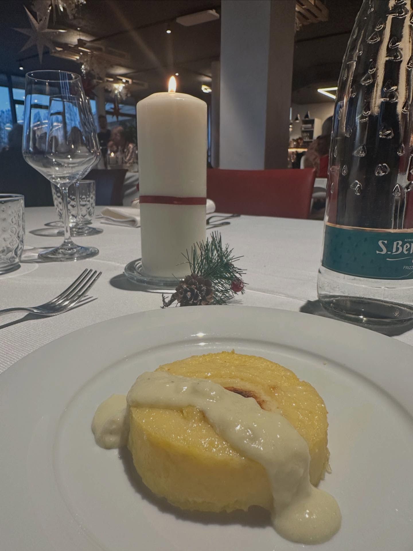 Un piatto con una torta di polenta e salsa alla panna, su una tavola apparecchiata per cenare con una candela.