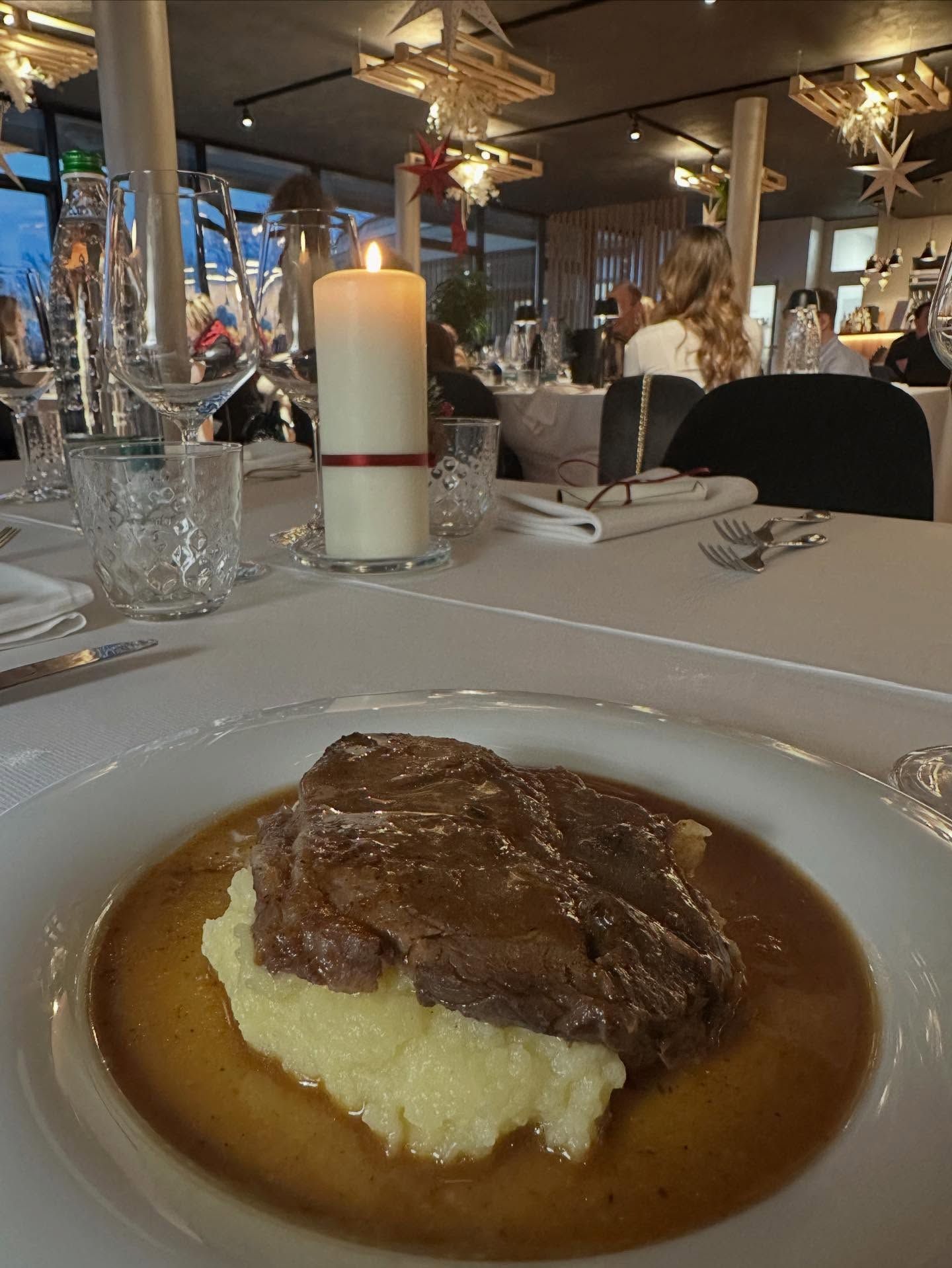 Piatto di manzo servito su un piatto bianco con purè di patate e salsa, servito in un ristorante con una candela accesa.