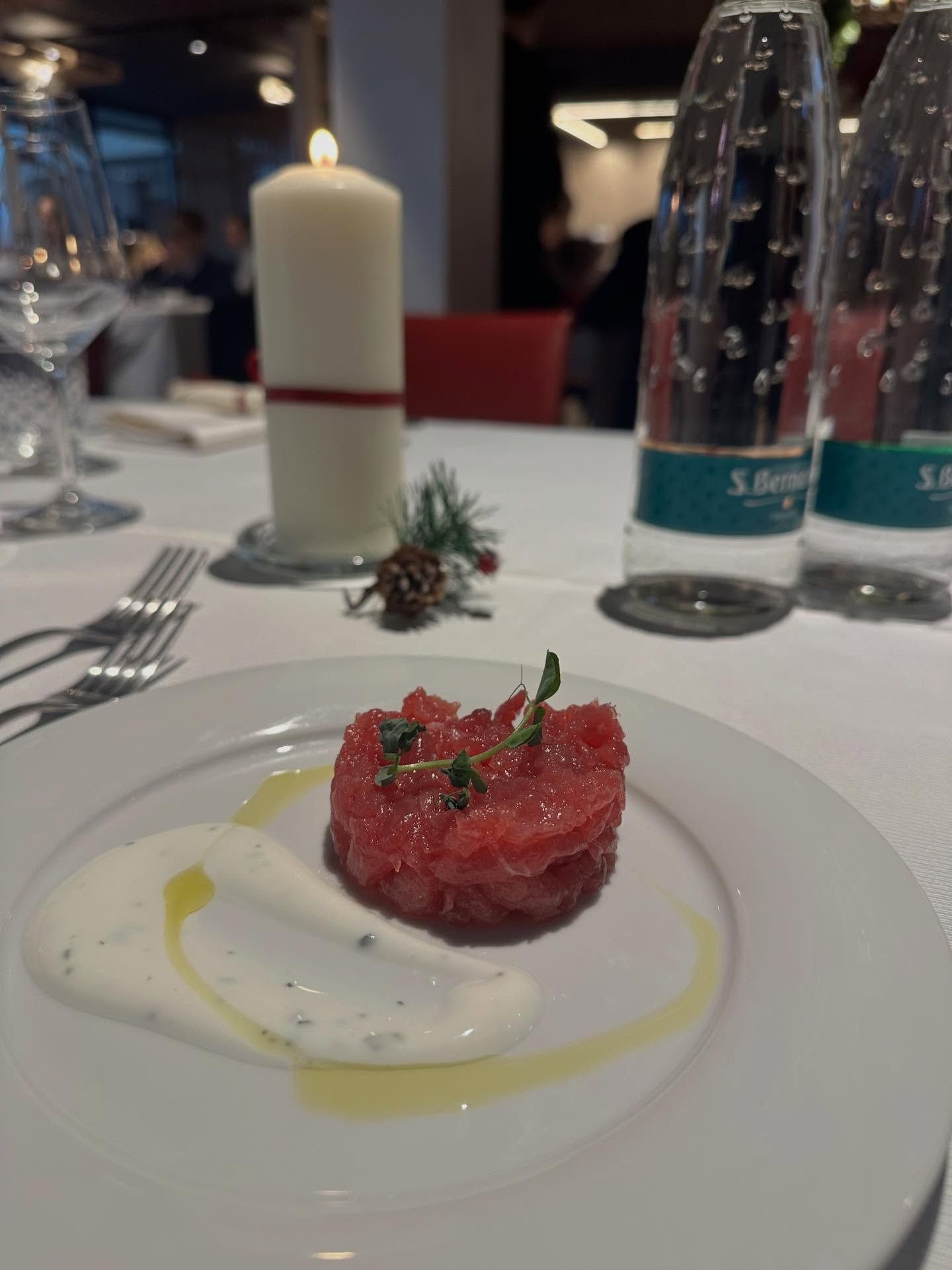 Un piatto con carne cruda, salsa e contorno, posto su un tavolo con una candela accesa e bottiglie d'acqua.