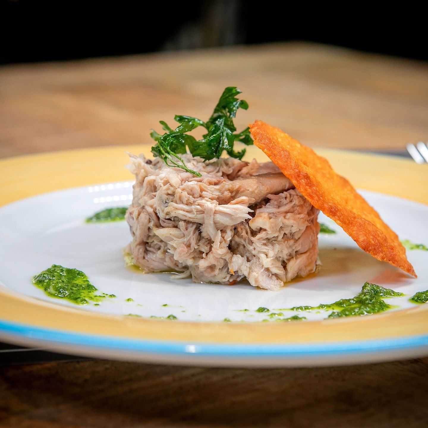 Piatto di carne sfilacciata guarnito con salsa verde e una fetta di pane tostato su un piatto.