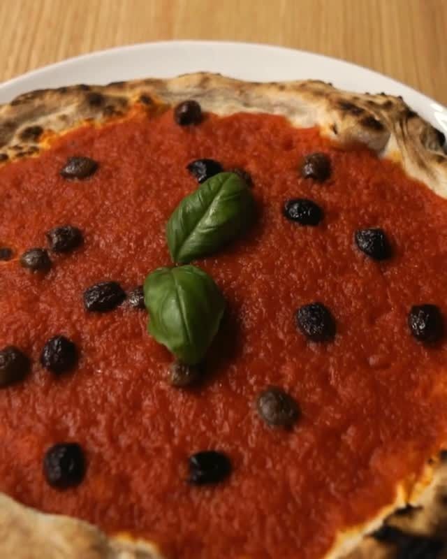 Pizza con salsa di pomodoro, olive e foglie di basilico su un piatto bianco.
