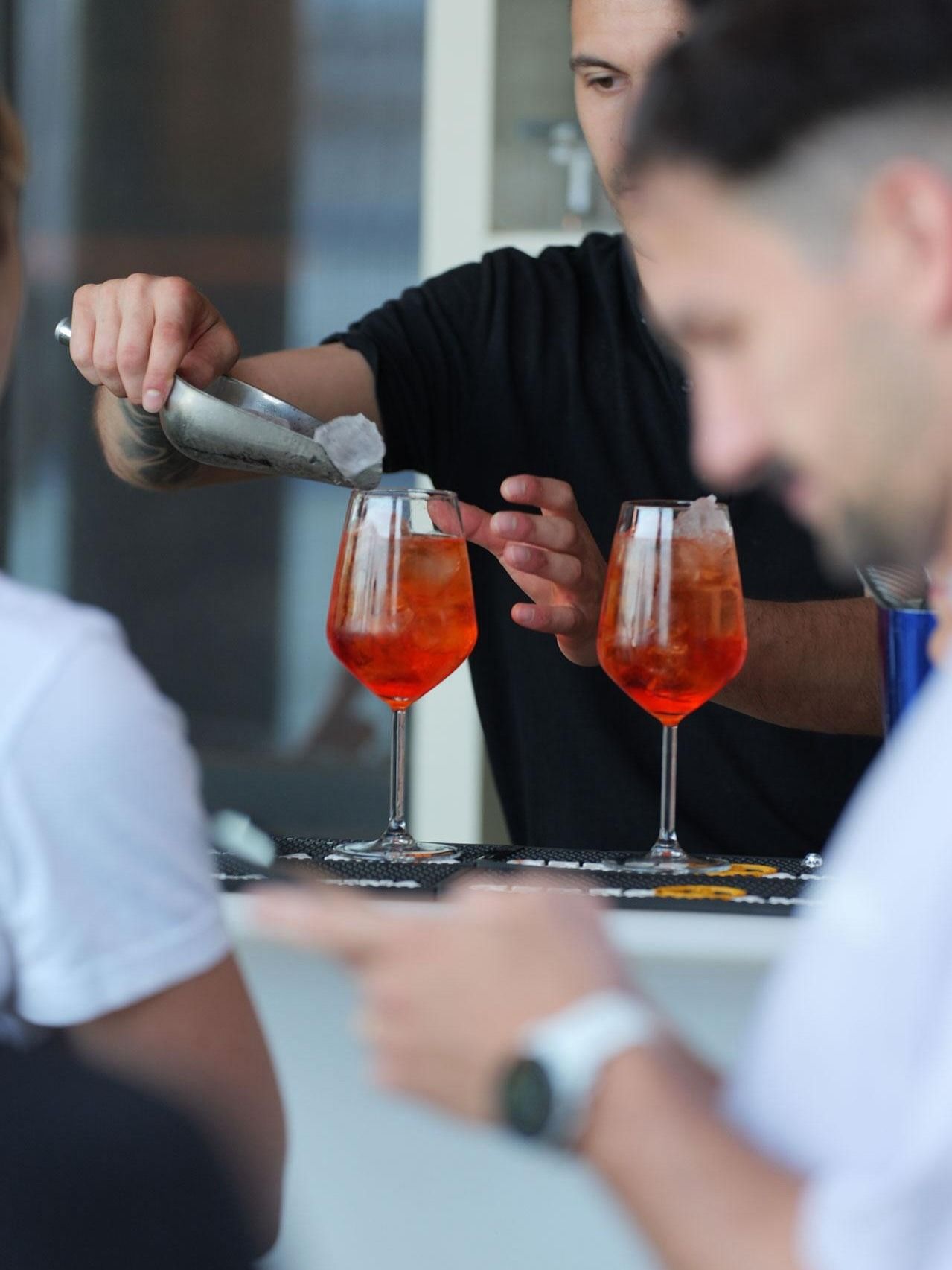 Il barista versa il drink in due cocktail all'arancia in bicchieri alti.