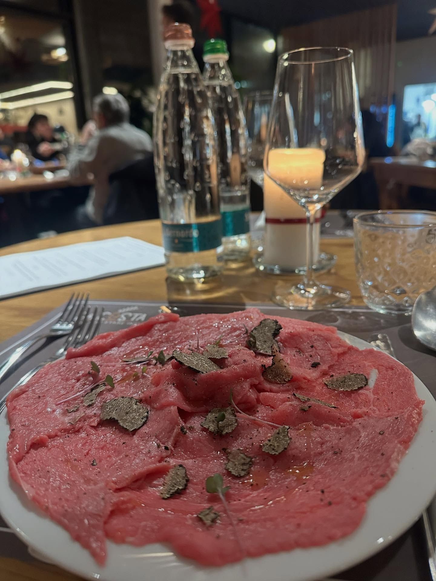 Carpaccio di manzo crudo tagliato sottile, guarnito con tartufo, servito su un piatto, al tavolo di un ristorante.