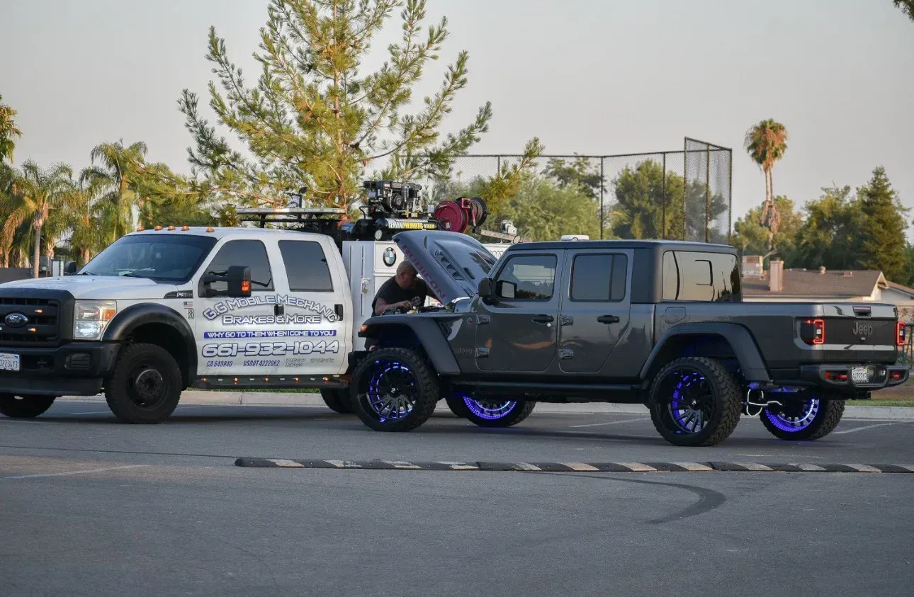 Two trucks parked on asphalt. A white truck with decals is next to a grey modified truck with blue underglow.