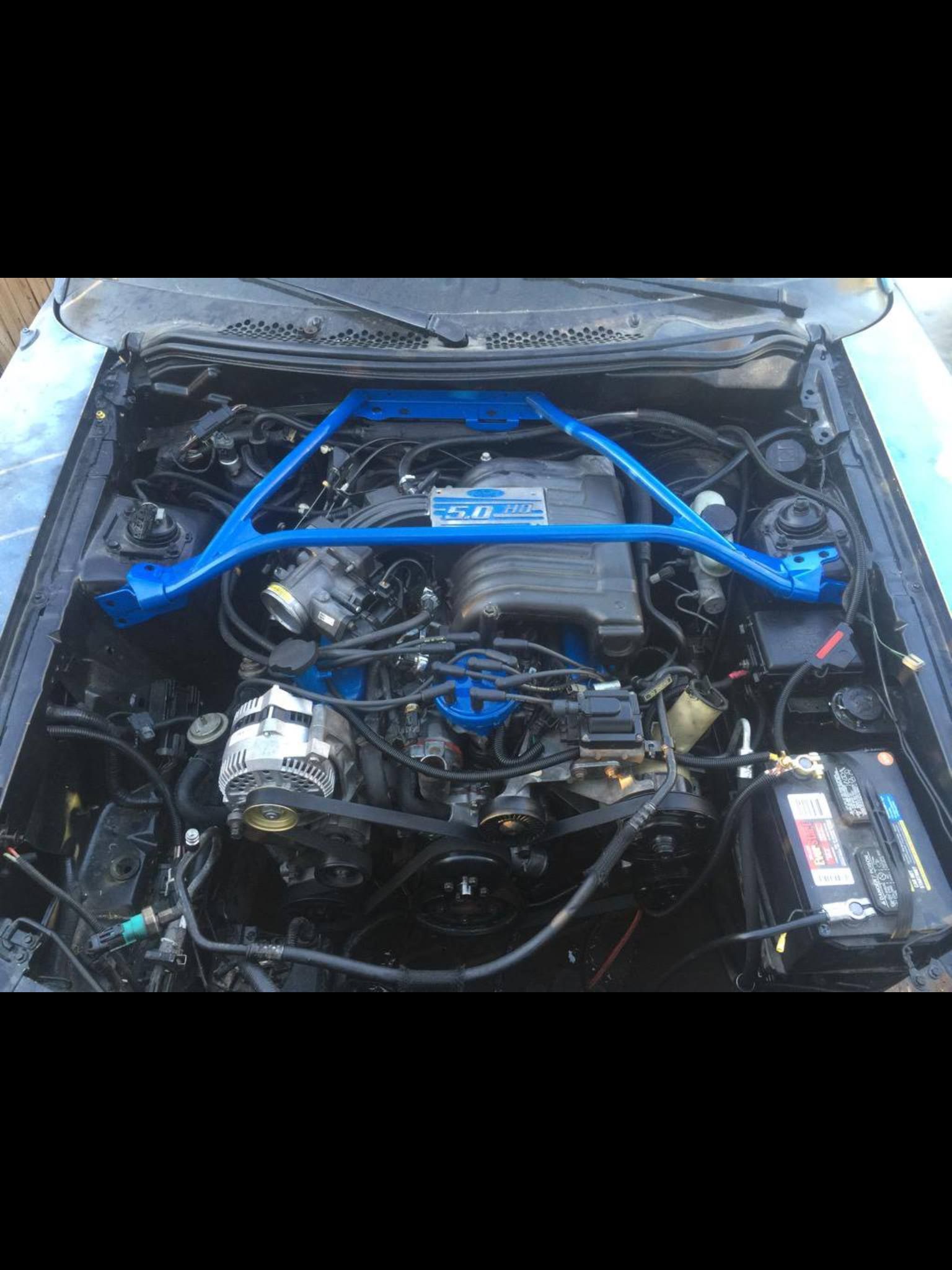 Blue engine bay of a classic car with a blue strut tower brace and black components.