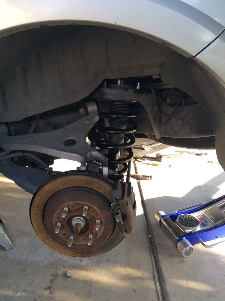 Rear car suspension being worked on. Tire removed, spring and shock visible.