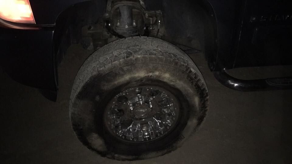 Flat, damaged tire on a dark-colored vehicle with a visible rim.