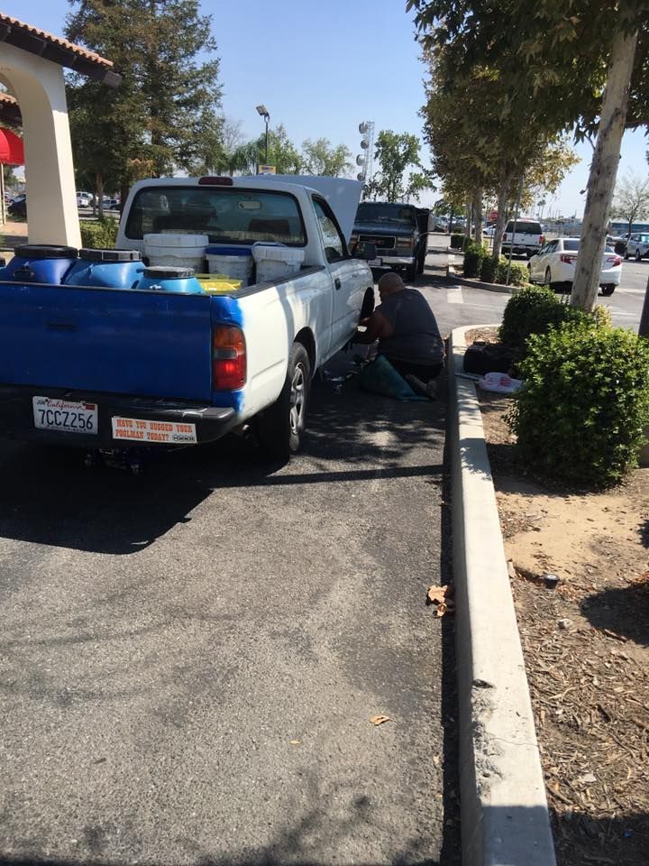 A person repairs a white and blue pickup truck in a parking lot.