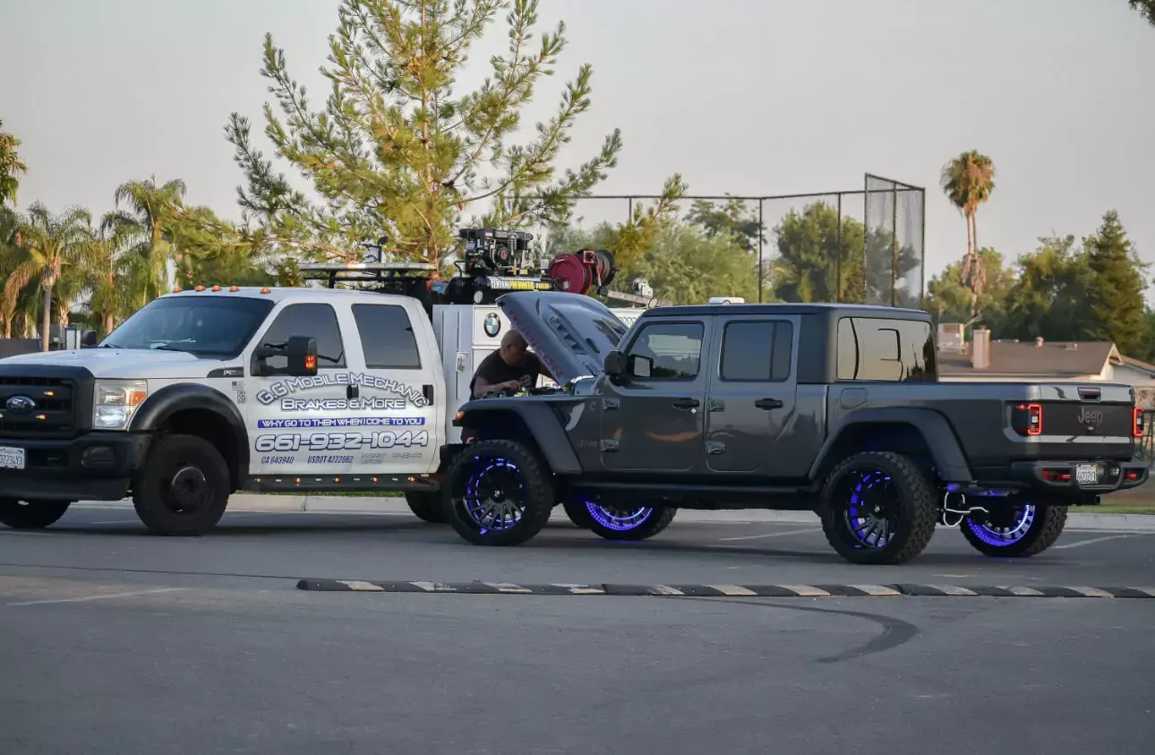 White tow truck and gray Jeep truck with custom wheels parked on pavement.