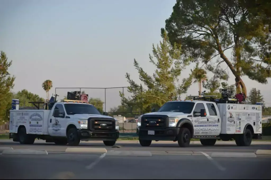 Two white service trucks parked on asphalt, outdoors. Trucks have company logos.