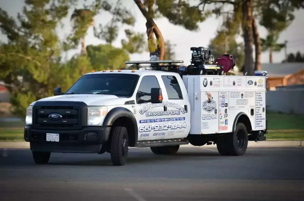 White service truck parked outside. Truck has logos, toolboxes, and equipment on top. Daytime.
