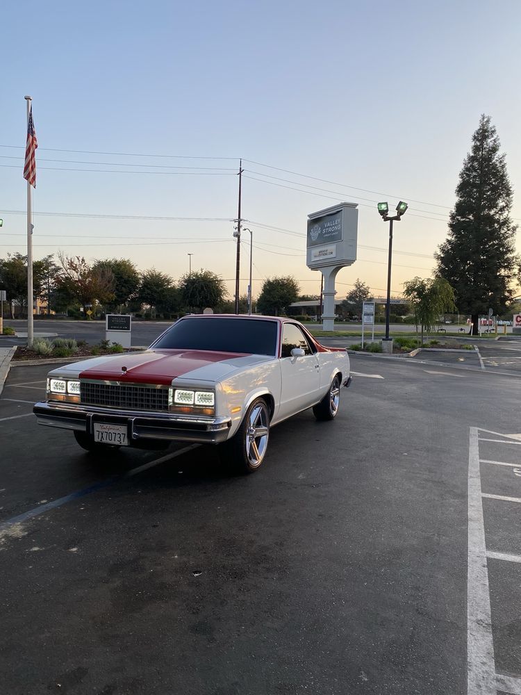 White and red classic El Camino car in a parking lot with an American flag.