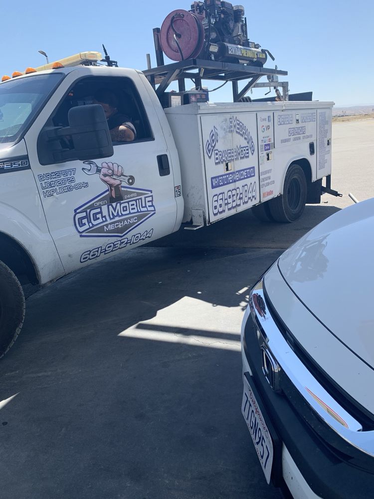 White service truck with a person in the driver's seat parked near a white car on pavement in a sunny setting.
